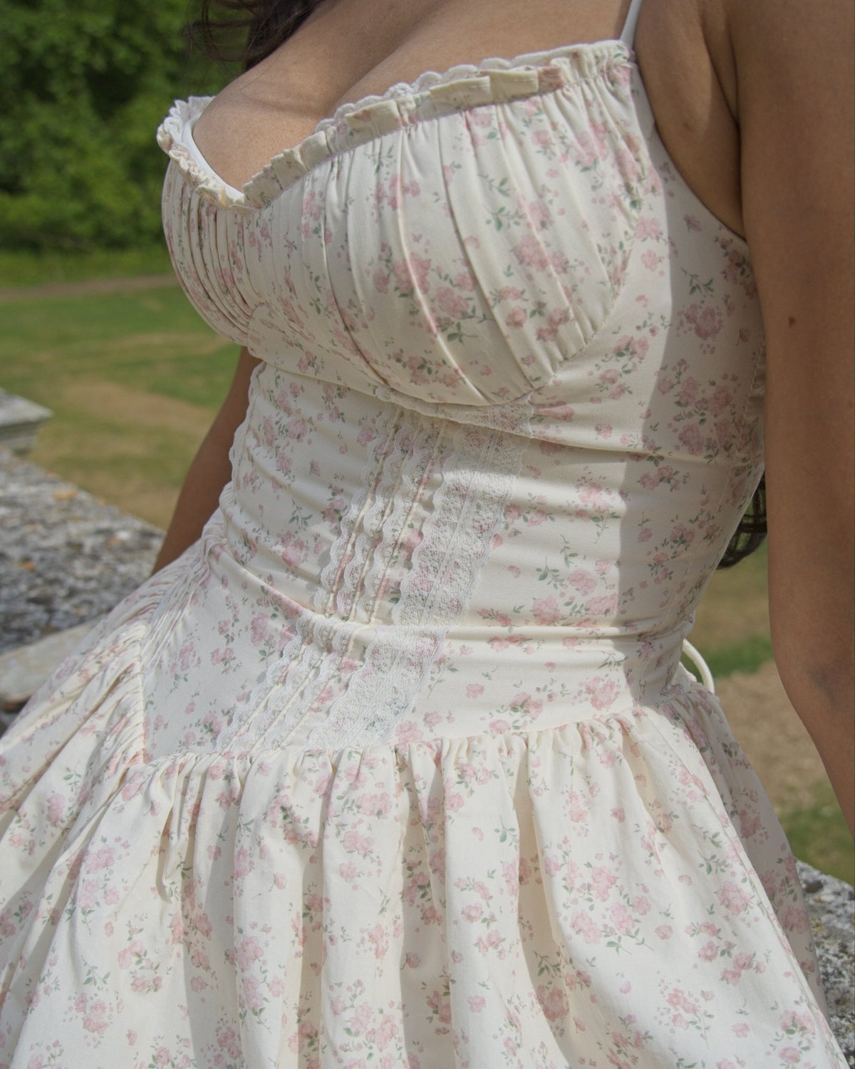 A close-up of a woman wearing a cream-colored spaghetti-strap dress with a pink and green floral print, featuring a gathered sweetheart neckline and a smocked bodice.
